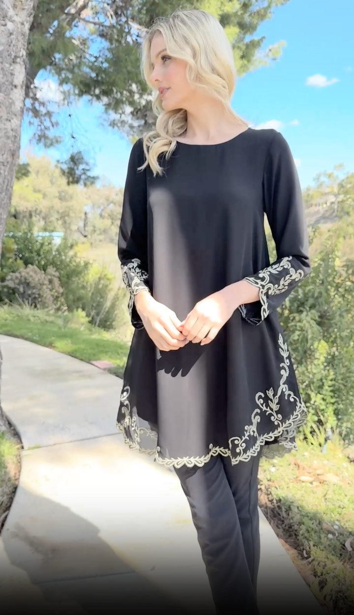 Woman outside looking to the side wearing Meena tunic in Black with black pants.