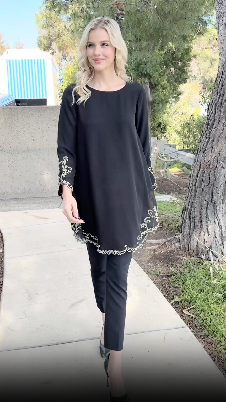 Woman walking outside wearing Meena tunic in Black with black pants and heels.