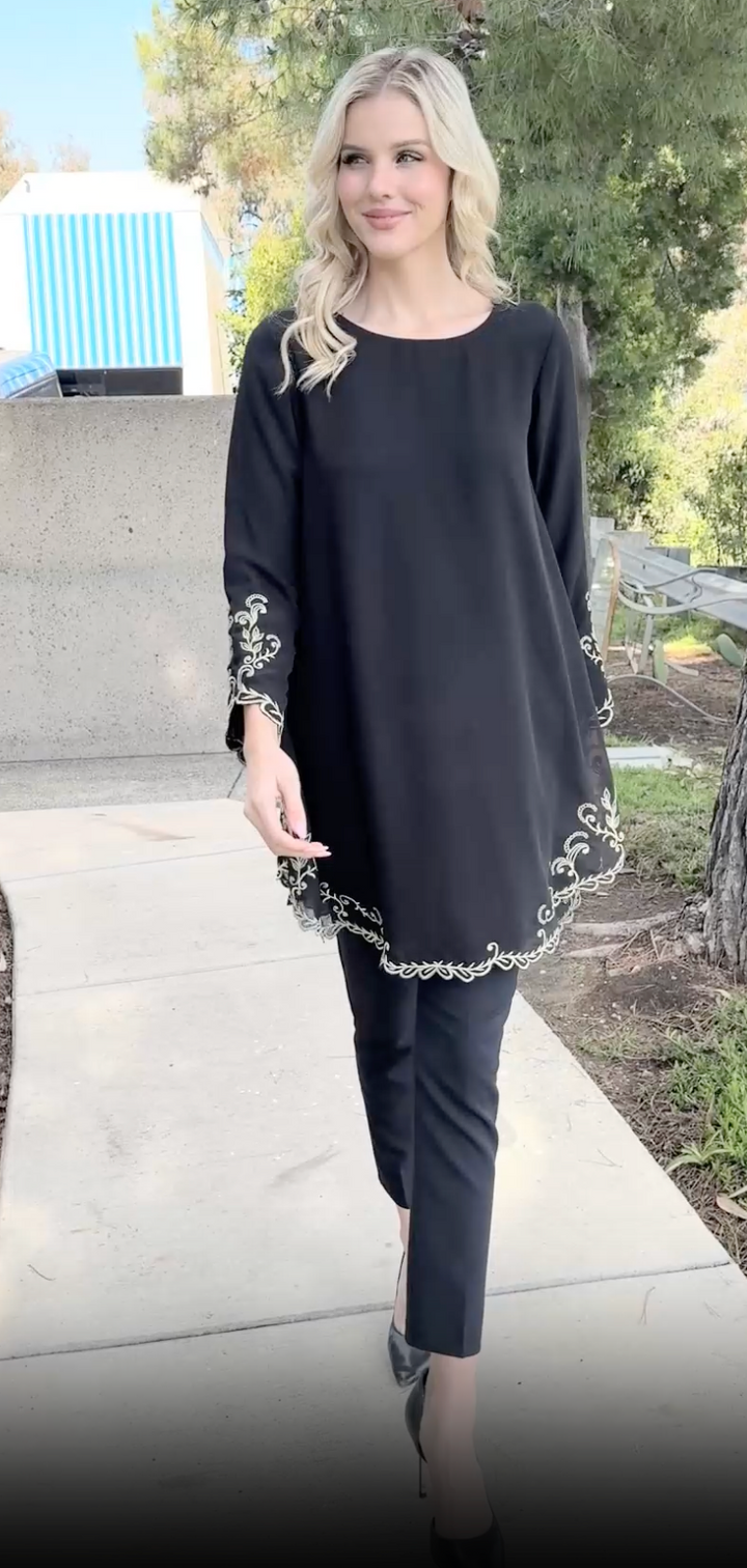 Woman walking outside wearing Meena tunic in Black with black pants and heels.