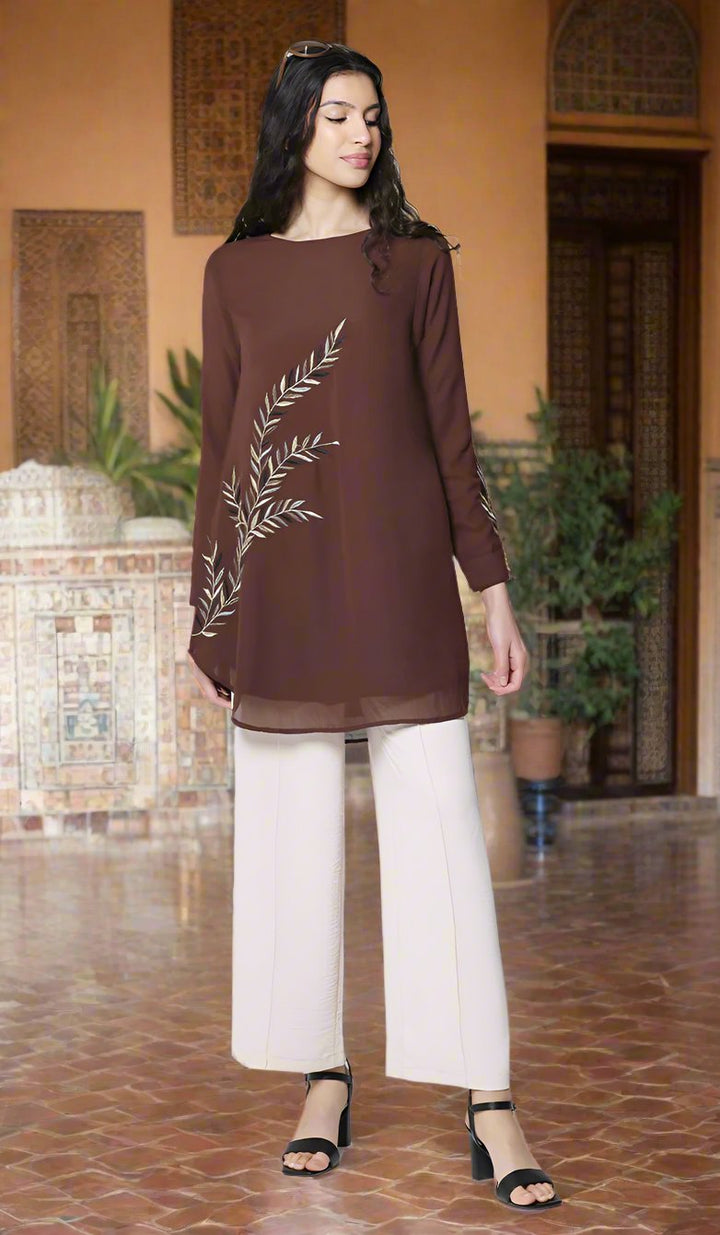 Woman standing outside of a building wearing Baraka tunic in Cocoa with white pants and heels.