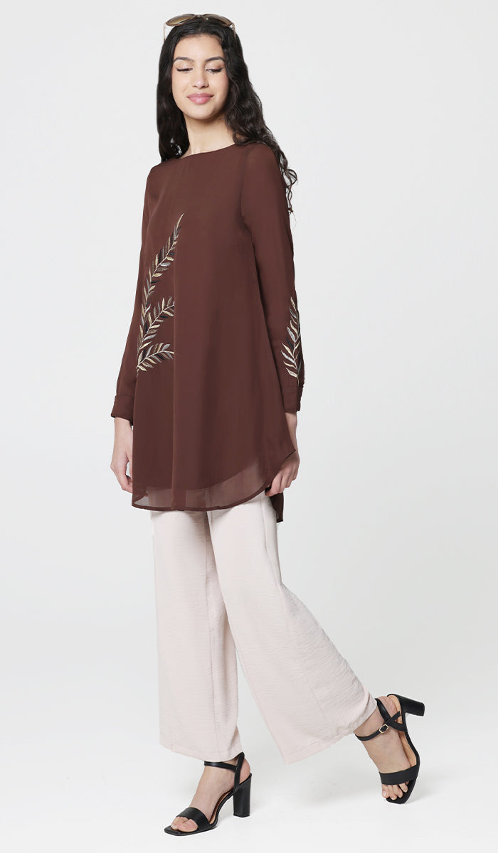 Side view of woman wearing Baraka tunic in Cocoa with white pants and heels.