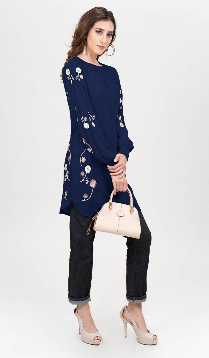 Model posing in embroidered navy blue Iman tunic with purse, jeans, and heels.