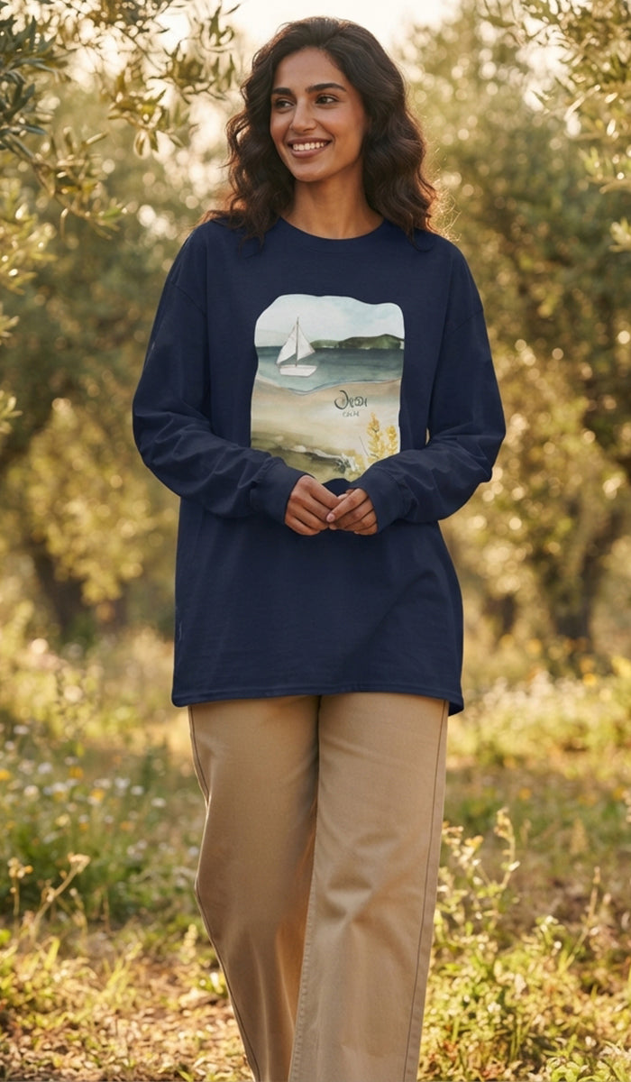 A woman wearing a navy blue long-sleeve t-shirt with a beach graphic print, paired with beige pants, standing outdoors in a sunny, blurred garden setting.