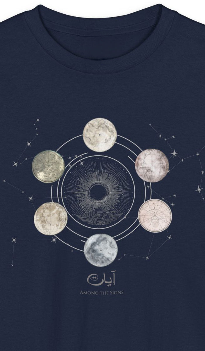 A close-up of a navy blue t-shirt featuring a celestial graphic of the moon phases in a circular orbit with Arabic calligraphy and the text 'AMONG THE SIGNS' printed below.