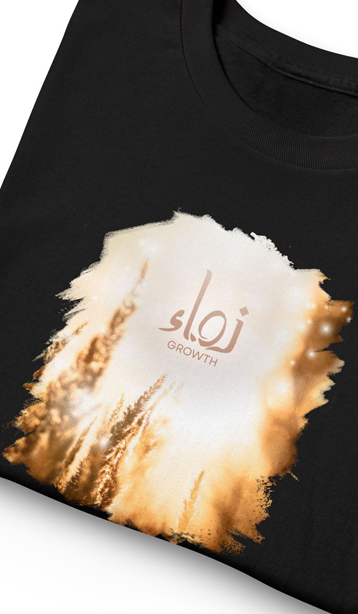 A close-up of a black t-shirt featuring a large graphic print of a golden wheat field with the text 'ZAWA GROWTH' printed in a warm beige and brown color.