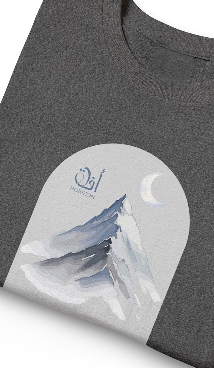 A close-up of a dark heather gray t-shirt featuring a circular graphic print of a snowy mountain peak under a crescent moon with Arabic calligraphy and the word 'HOMORIC' printed below it.