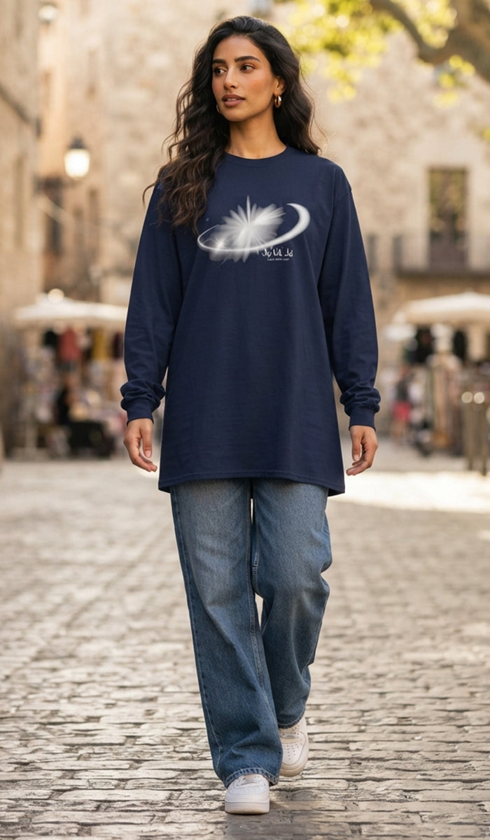 A woman walking on a cobblestone street wearing a navy blue long-sleeve t-shirt with a white graphic print of a sun and crescent moon, paired with wide-leg blue jeans and white sneakers.