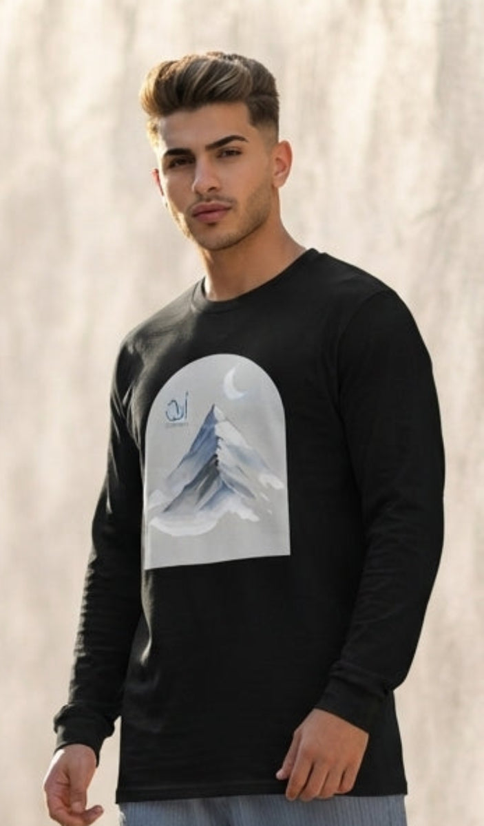 A man wearing a black long-sleeve t-shirt with a white graphic print on the front, paired with wide-leg light blue jeans and white sneakers, standing outdoors against a textured beige wall.