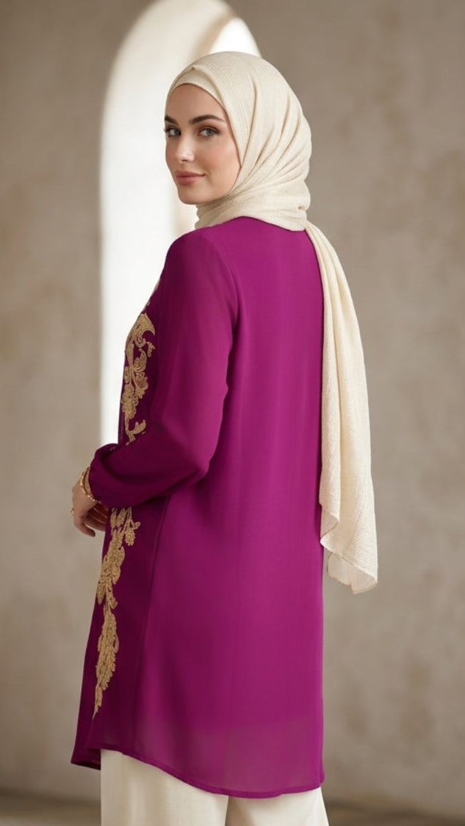 Woman wearing a magenta top with gold embroidery and a beige hijab against a neutral background