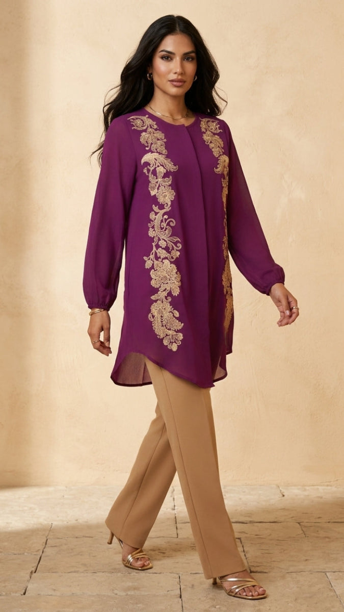 Woman wearing a purple embroidered top and beige pants on a beige background