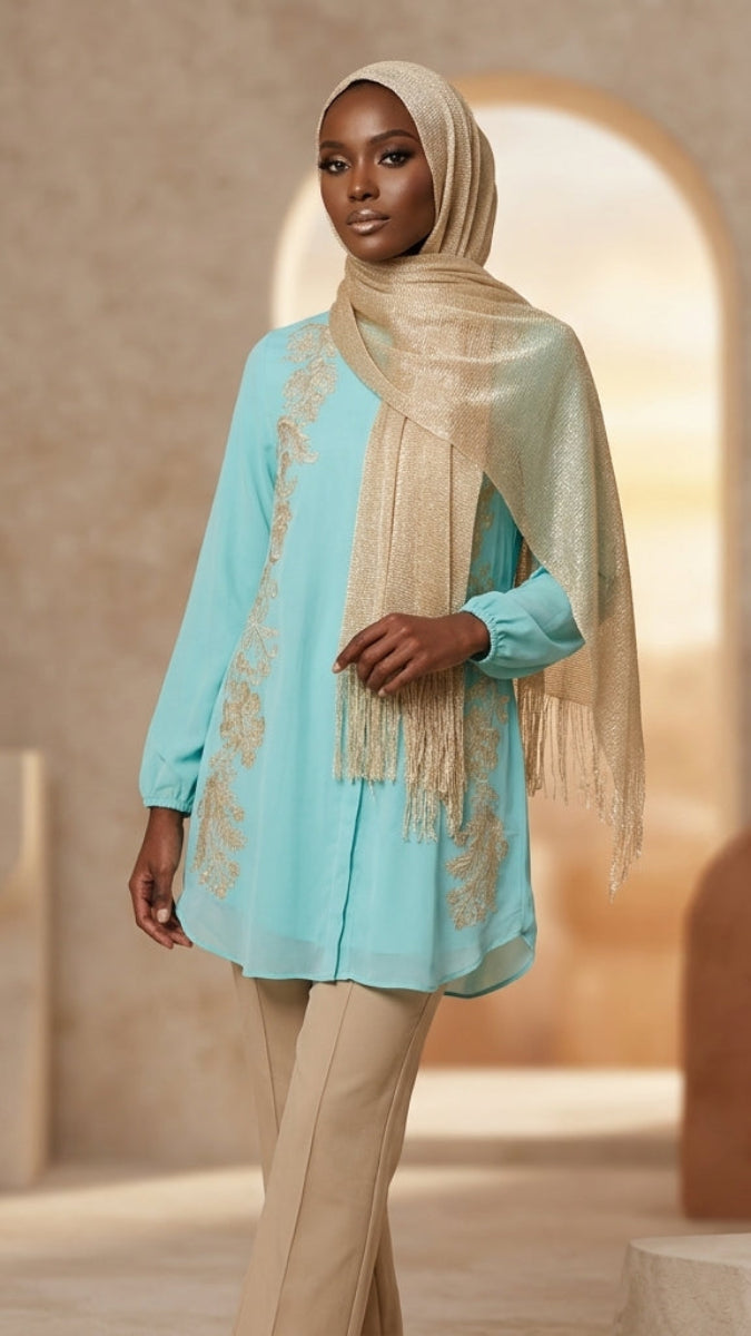 Woman wearing a light blue top with lace details and beige hijab in a warm-toned setting