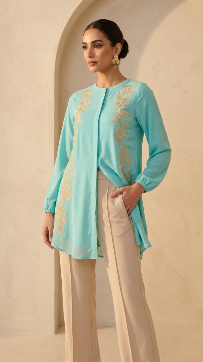Woman wearing a light blue embroidered top and beige pants against a beige background