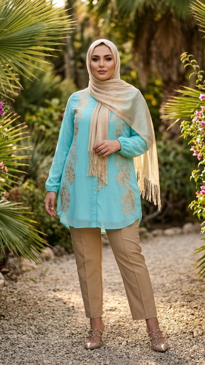 Woman in a turquoise top and beige pants with a matching scarf standing in a garden.