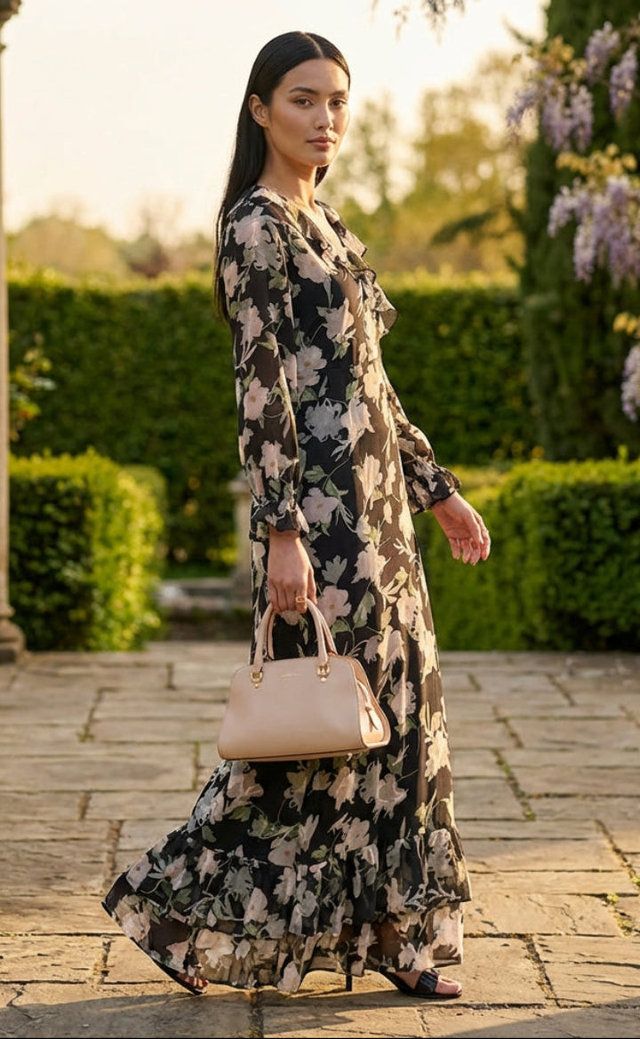 Woman in a floral dress holding a beige handbag in a garden setting