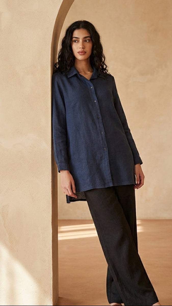 Woman wearing a dark blue shirt and black pants standing in a sunlit room with arched doorways.