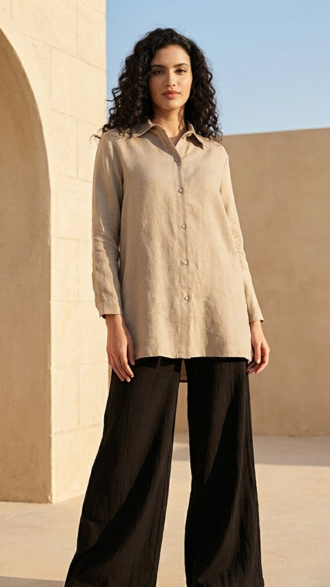 Woman wearing a beige shirt and black pants standing in a sunlit outdoor setting with arches and a palm tree.