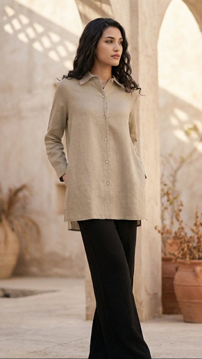 Woman wearing a beige shirt and black pants in an outdoor setting with stone arches and potted plants.