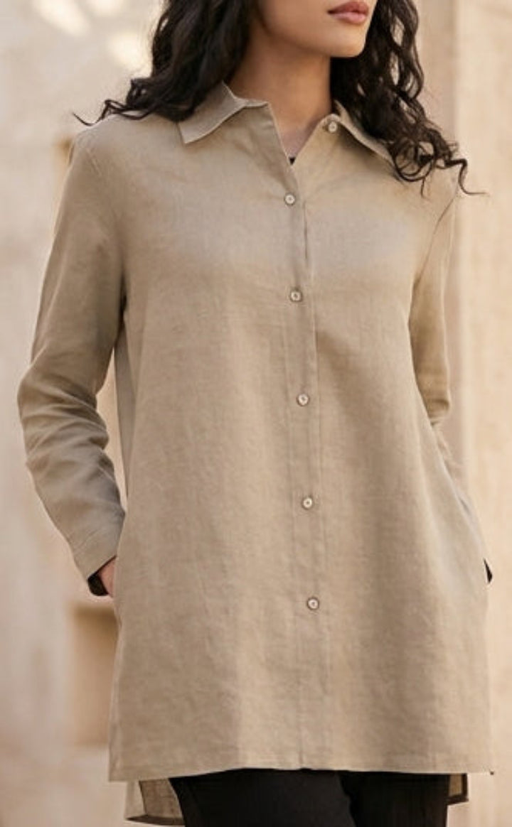 Woman wearing a beige shirt and black pants in an outdoor setting with stone arches and potted plants.