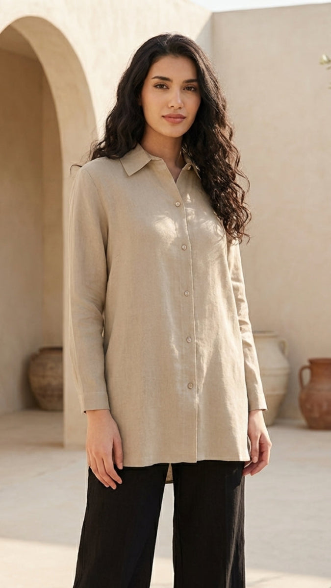Woman wearing a beige shirt and black pants standing in a sunlit outdoor setting with arches and vases.