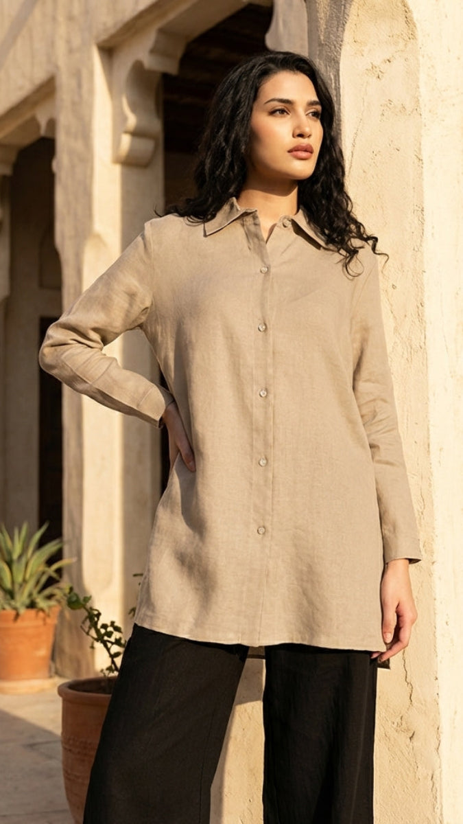 Woman wearing a beige shirt and black pants standing in front of a building with plants.