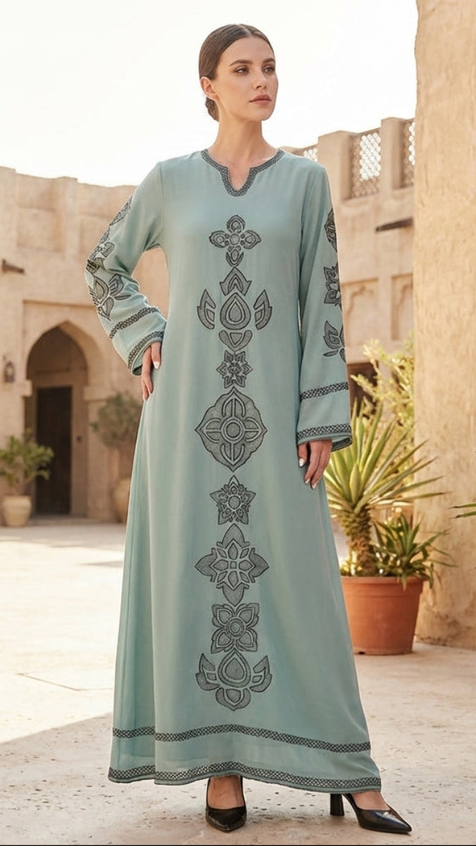 Woman in a long, light blue dress with intricate patterns standing in front of an architectural background.
