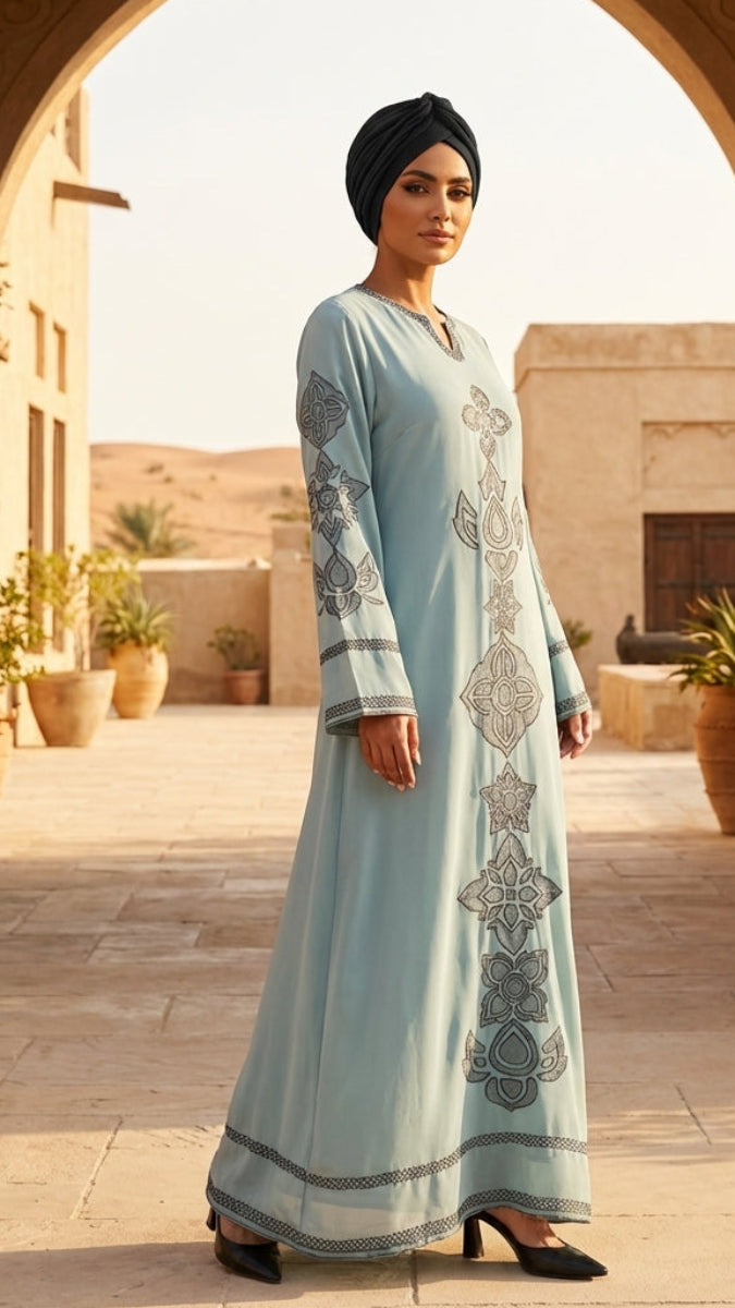 Woman in a light blue dress with intricate patterns standing in front of an archway with desert scenery.