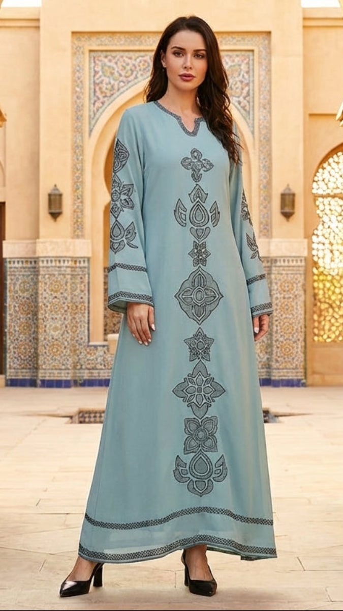 Woman in a light blue dress with intricate patterns standing in an ornate architectural setting.
