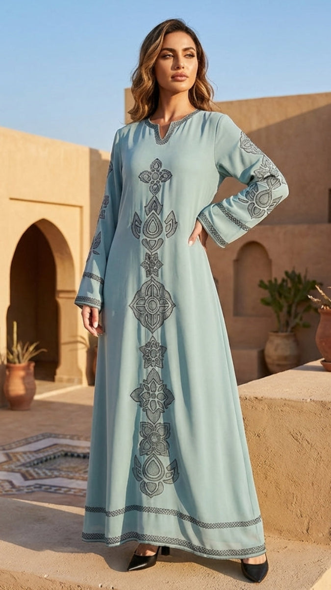 Woman in a long light blue dress with patterns standing in front of a traditional building.