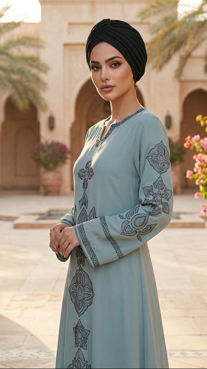 Woman in a light blue embroidered dress standing in a courtyard with palm trees and flowers.