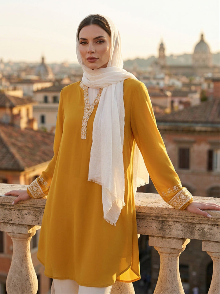 Woman in a yellow dress with a white scarf standing on a balcony with a cityscape in the background