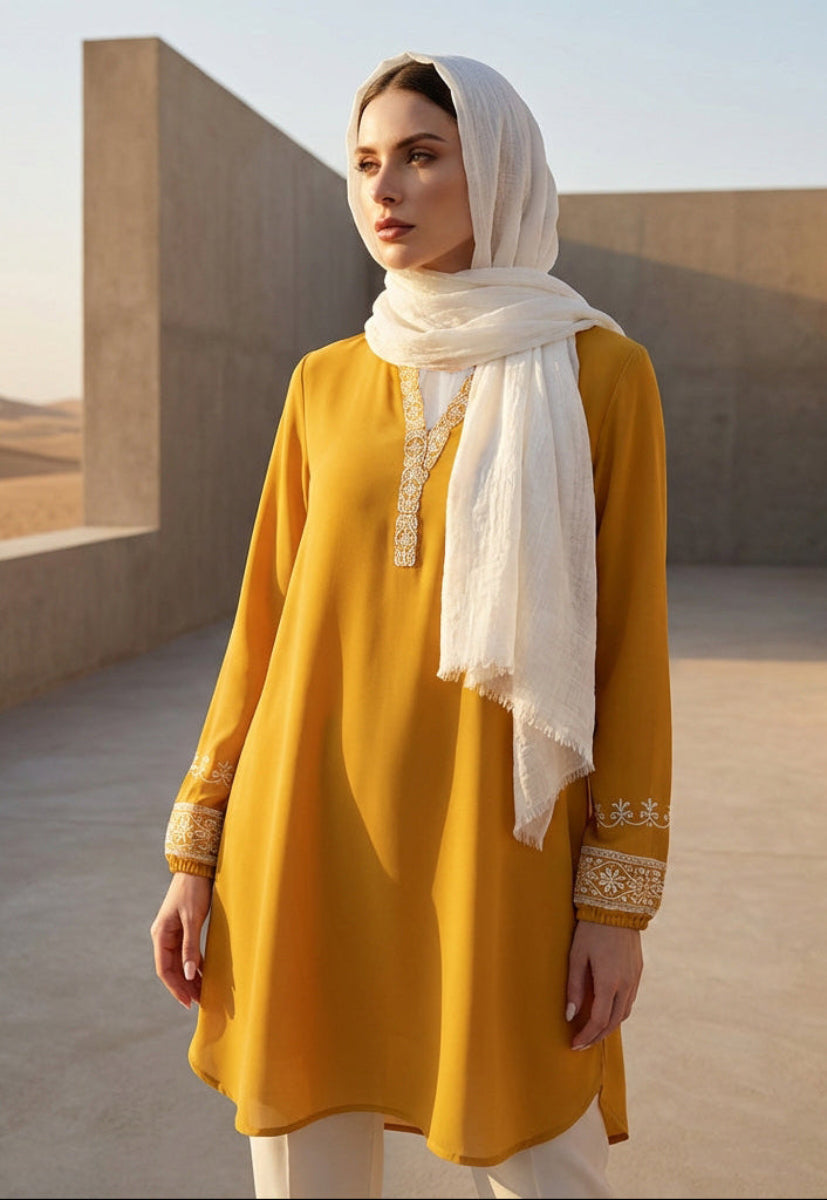 Woman in a yellow dress with a white scarf standing in a desert setting.