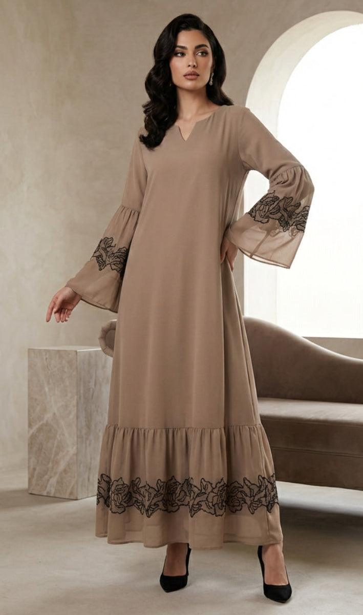 Woman wearing a beige dress with black lace details in a room with a beige wall and chair.