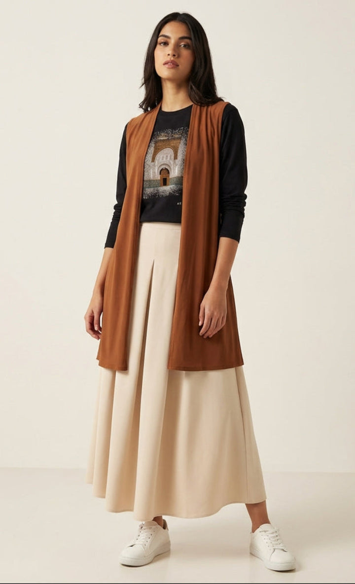 Woman wearing a long brown cardigan over a black top and beige skirt on a white background
