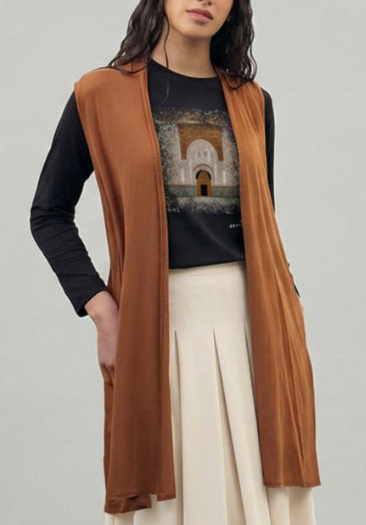 Woman wearing a brown vest, black top, beige pants, and white shoes on a gray background