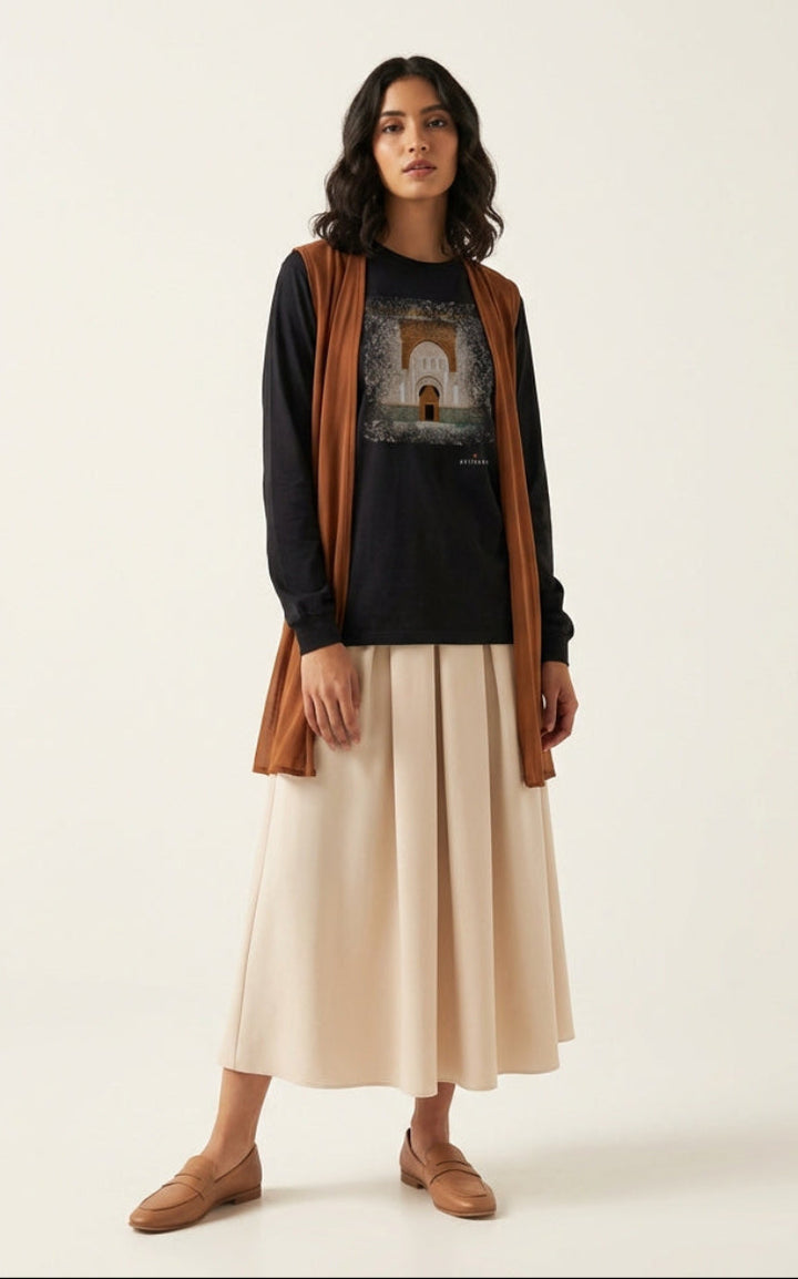 Woman wearing a black shirt with a graphic design, brown cardigan, beige skirt, and brown shoes on a white background