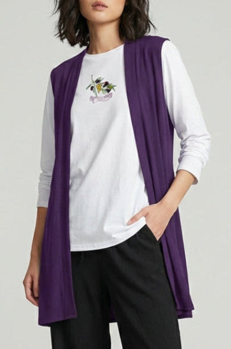 Woman wearing a white shirt with a purple vest and black pants on a gray background