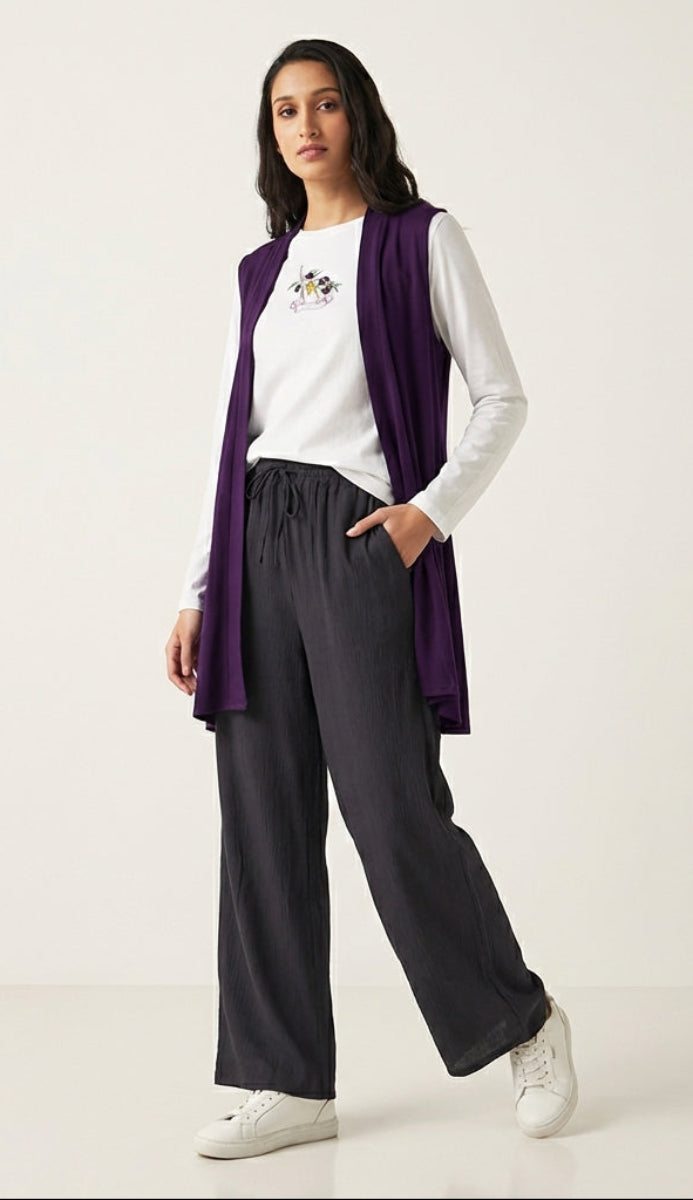 Woman wearing a purple cardigan, white shirt, black pants, and white sneakers on a white background