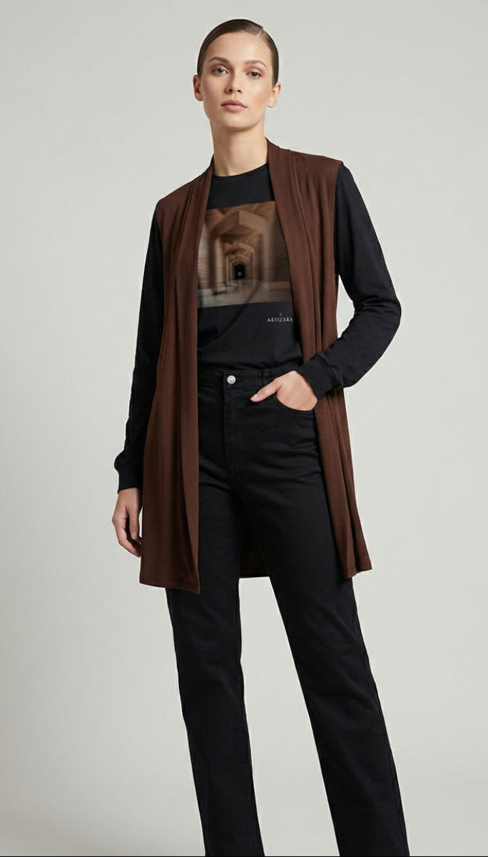 Person wearing a brown vest over a black shirt with a graphic design, paired with black pants on a light gray background.