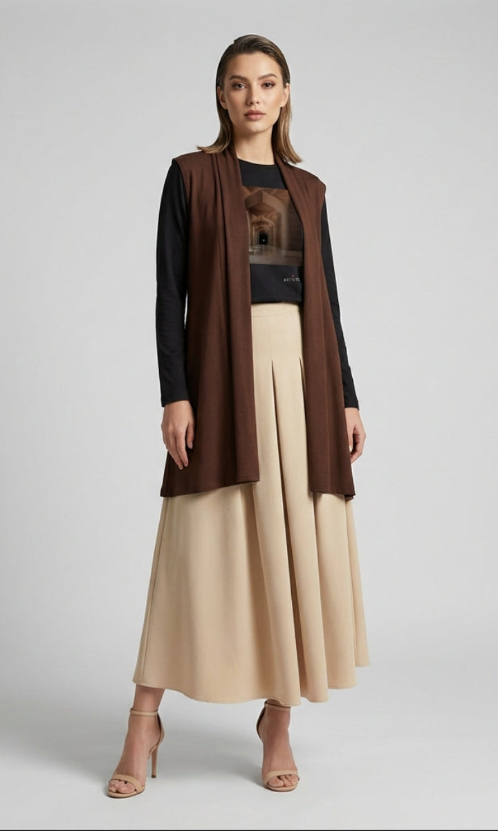 Woman wearing a brown long coat over a black top and beige skirt on a gray background