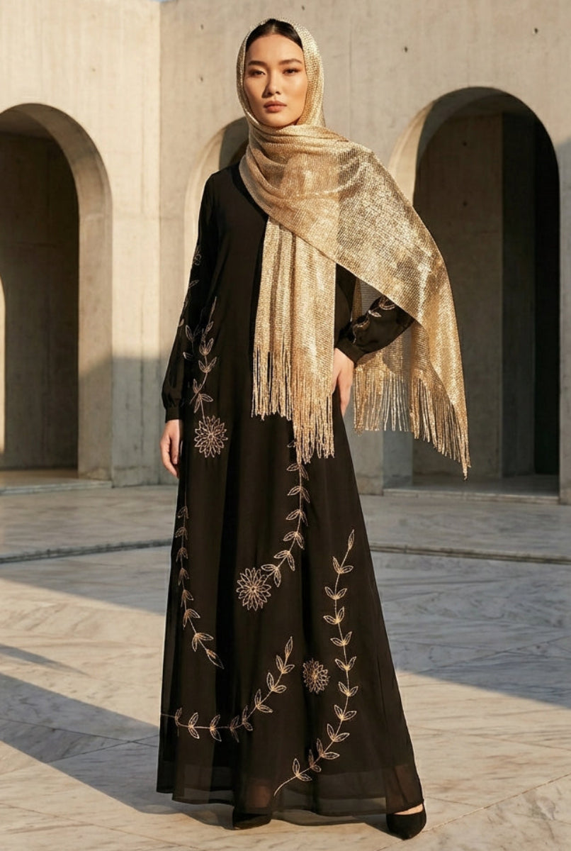 Woman in a black embroidered dress with a beige scarf standing in front of stone arches.