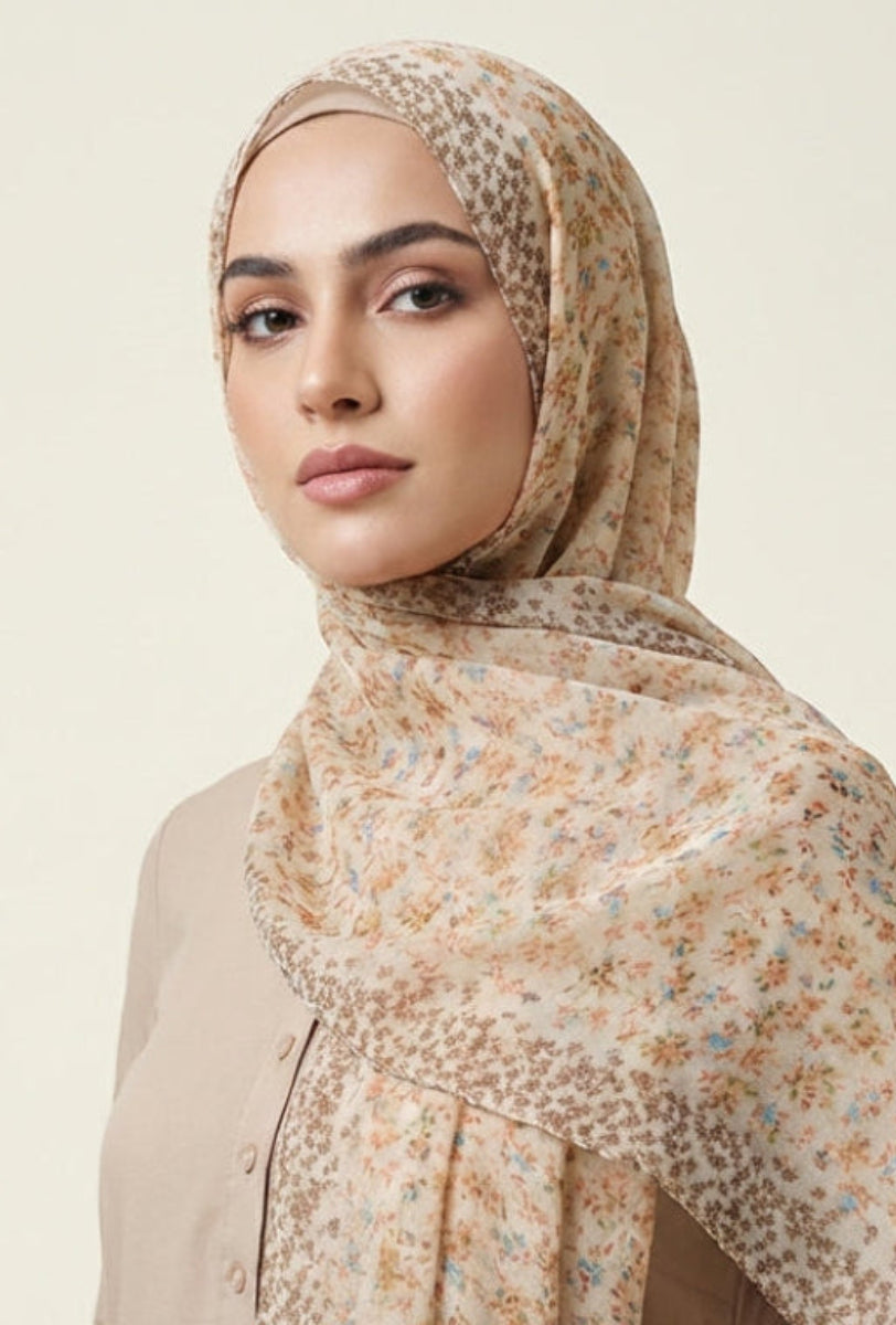 Woman wearing a beige floral hijab against a plain background