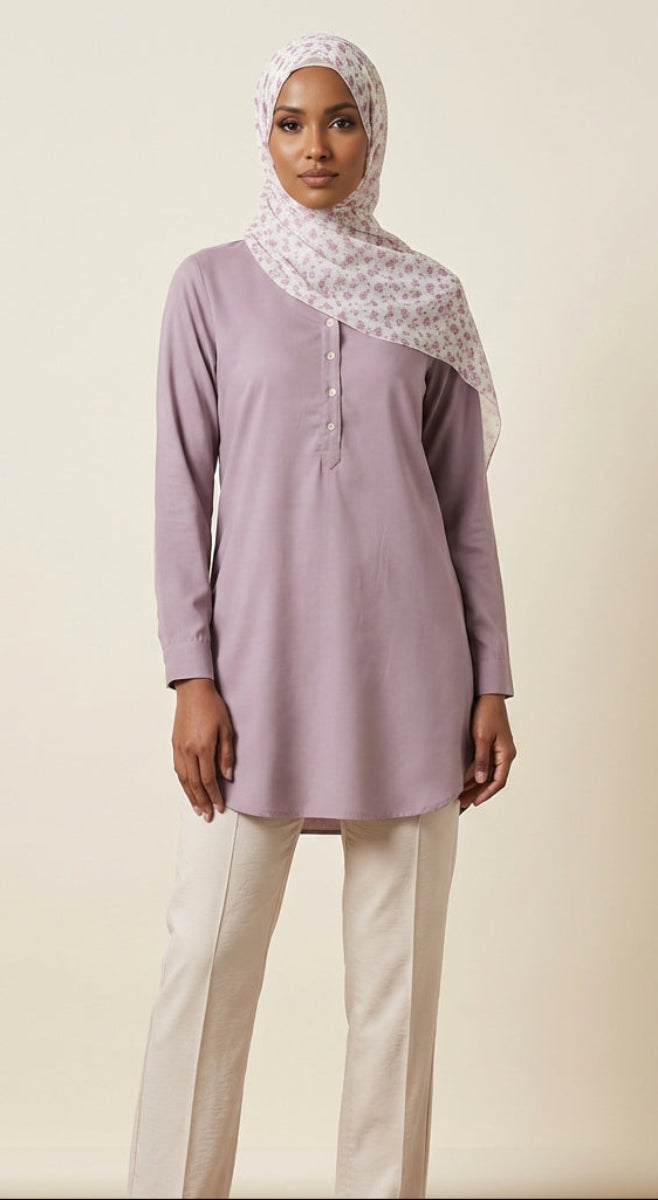Woman wearing a light purple long-sleeve top and white pants with a patterned hijab on a beige background