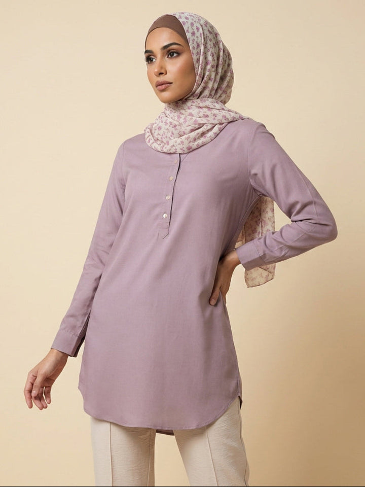 Woman wearing a light purple long-sleeve top and patterned hijab on a beige background