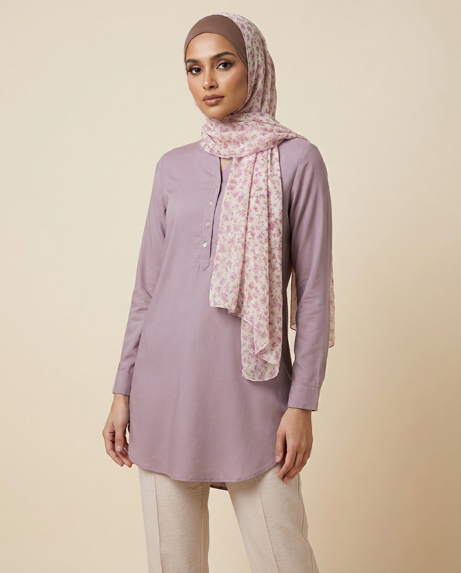 Woman wearing a light purple long-sleeve top and beige pants with a patterned scarf on a beige background