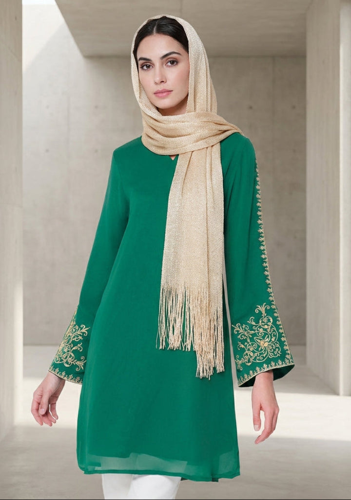 Woman wearing a green embroidered dress with a beige scarf in a neutral setting