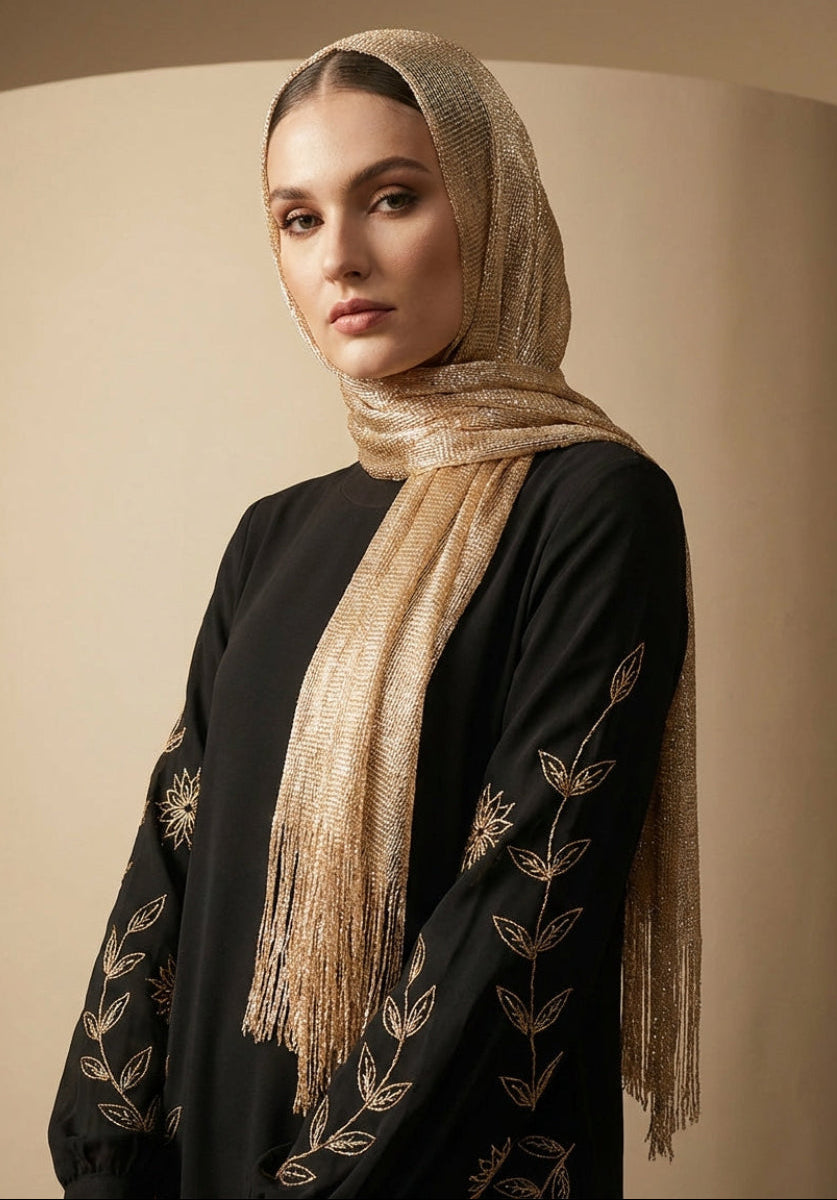 Woman wearing a black outfit with gold embroidery and a beige hijab against a beige background