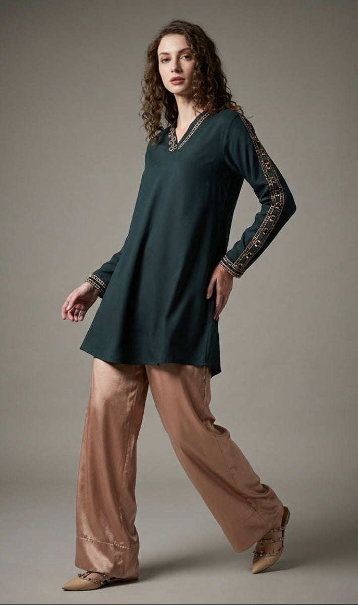 Woman wearing a dark green dress with patterned sleeves and beige pants on a gray background
