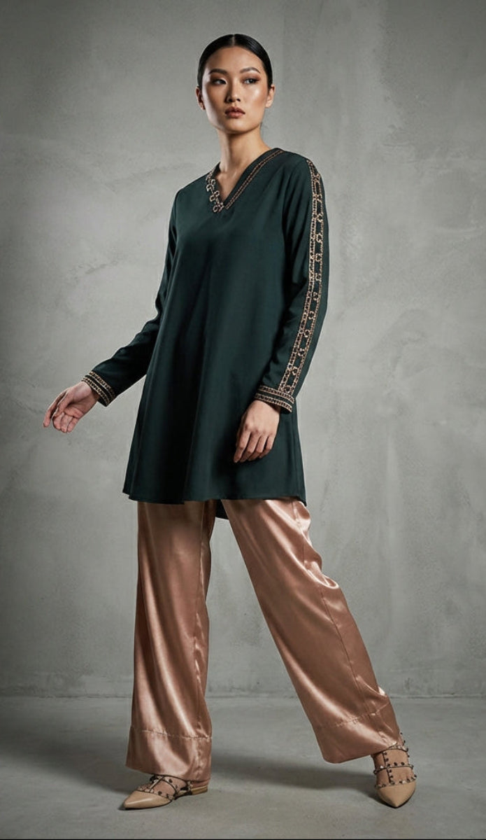 Woman wearing a dark green top and beige pants in a studio setting