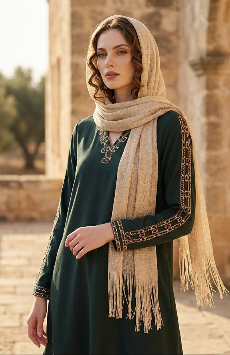 Woman wearing a green dress and beige scarf standing in front of stone architecture.