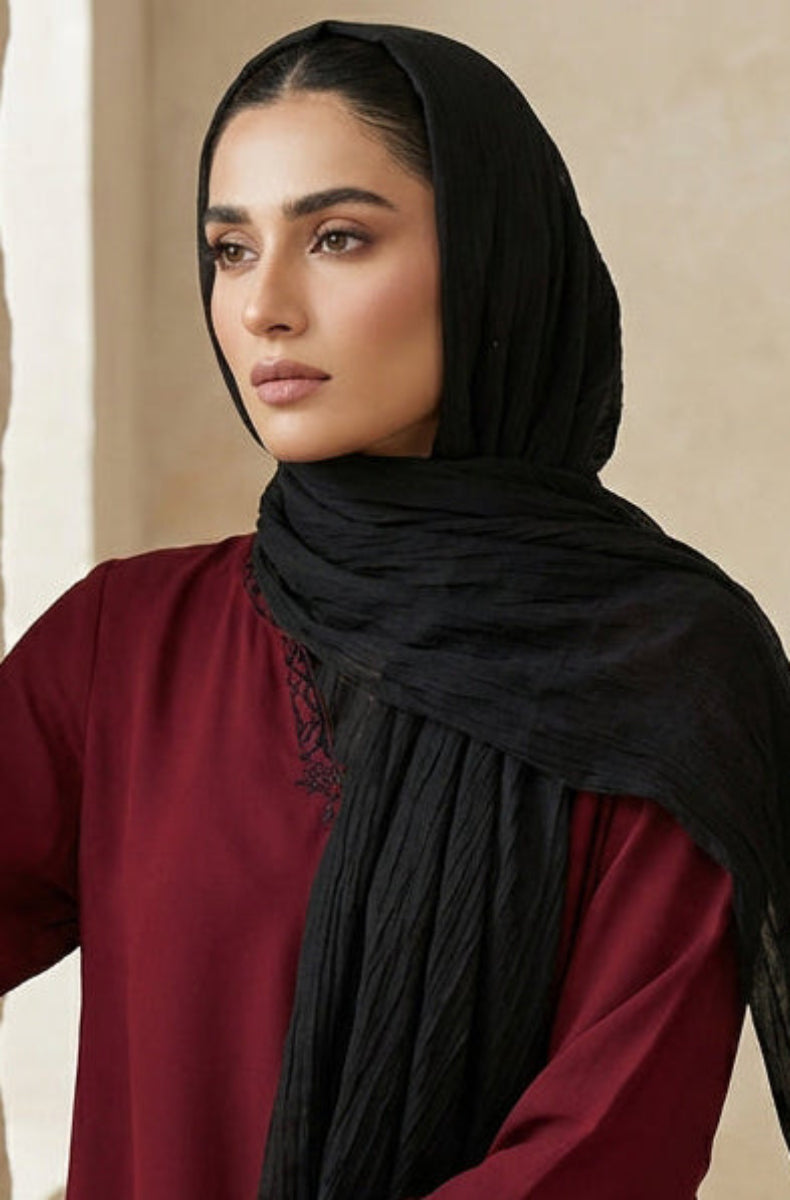 Woman wearing a black hijab and red outfit against a beige wall with a vase.